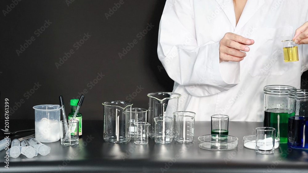 Fototapeta premium Scientist in White Lab Coat Holding Beaker with Yellow Liquid in Laboratory