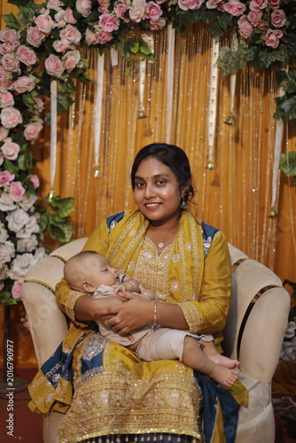 Tablou pe pânză Smiling South Asian aunt holding her sleeping baby nephew at a festive cultural event