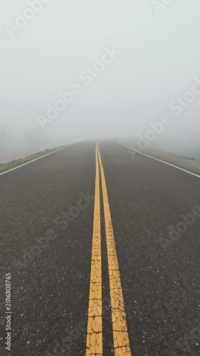 Vertical shot of a mysterious asphalt road disappearing into thick heavy fog