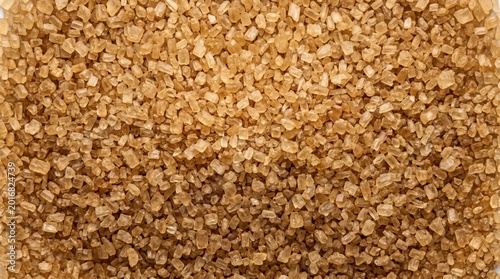 Close-up macro view of granular brown sugar crystals, revealing their irregular shapes and warm amber tones, baking, sweetening, or textural background applications