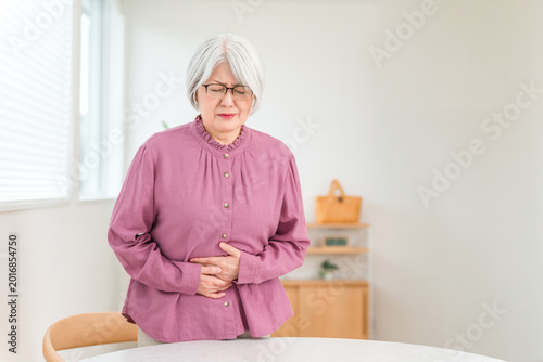 Bild auf Leinwand A senior woman with gray hair, clutching her stomach in pain, has a pained expression on her face