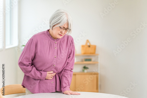 Obraz na płótnie A senior woman with gray hair, clutching her stomach in pain, has a pained expression on her face