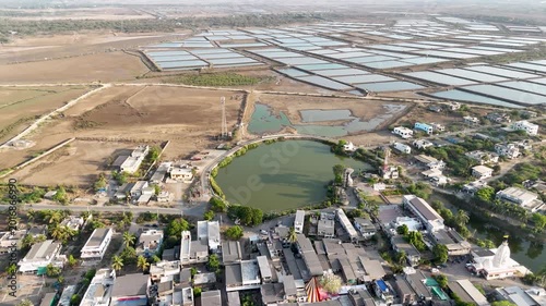 A breathtaking aerial view of expansive salt evaporation ponds spread across a dry coastal landscape near a rural village.