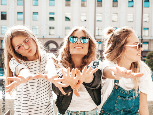 Portrait of three young beautiful smiling hipster in trendy summer clothes. Sexy carefree women posing on the street background.Positive models having fun in sunglasses.show their palms