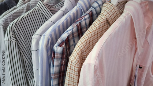 Selection of various mens button down shirts with patterns and stripes hanging on a clothing rack in a retail store for professional business casual fashion style