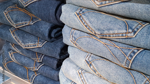 Stacked folded denim jeans trousers with focus on back pocket stitching detail and textile texture in a clothing store display for fashion retail concept