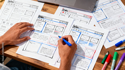 Designer sketching website wireframes on paper with colorful markers, illustrating early UI/UX planning and development