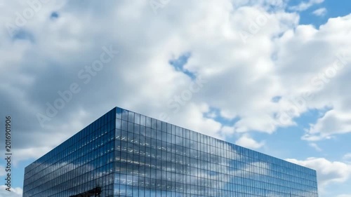 Modern glass office building reflects blue sky with white clouds while showcasing business architecture