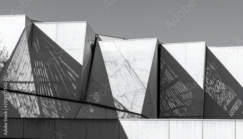 Abstract geometry of modern architecture bathed in high-contrast sunlight, showcasing intricate shadow play across angular facades and creating a compelling monochromatic visual rhythm