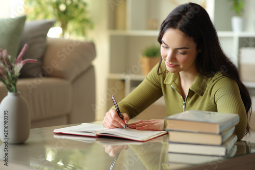 Serious young woman writing notes in paper agenda at home