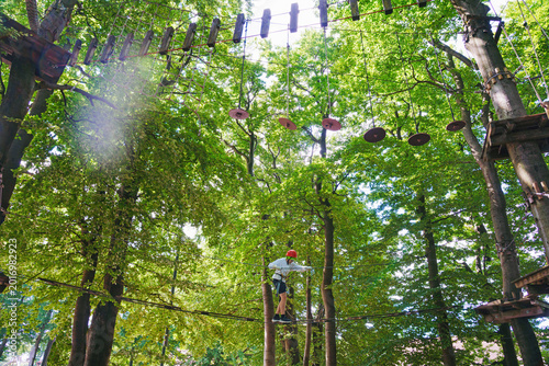 An active hobby in nature. A happy child enjoying an activity at a high ropes course on a summer day.