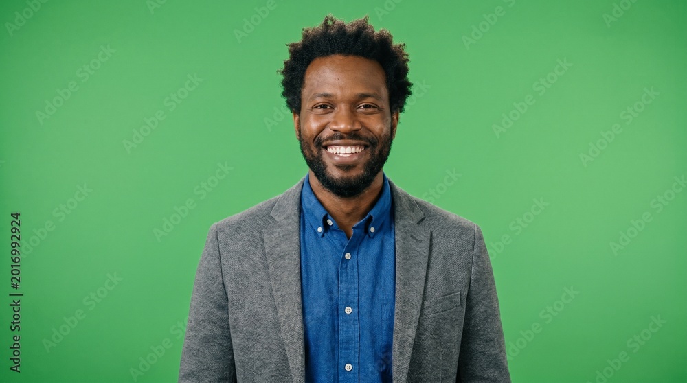 Fototapeta premium Distinguished man in a grey suit jacket and blue shirt smiling broadly on green screen background for academic leadership university recruitment and professional mentoring digital content