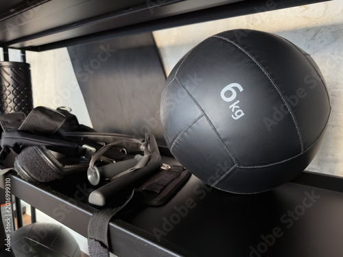 Obraz na plátně Black 6kg medicine ball on a gym shelf with functional training equipment and concrete wall