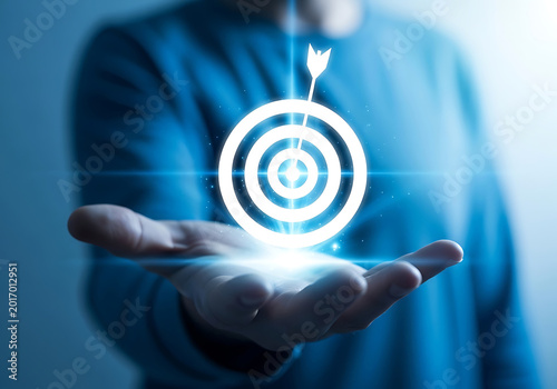 Person holding glowing target with arrow hitting bullseye, The image uses a cool blue color palette and conveys a sense of focus and achievement.