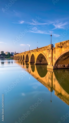 A serene landscape of an old stone bridge over calm water