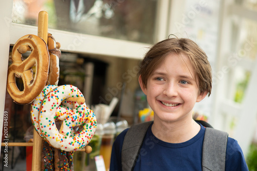  Portrait of a smiling boy with backpack standing near traditional pretzels display in outdoor market