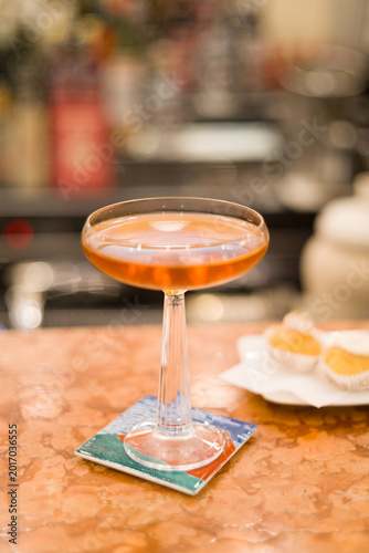 Elegant and sophisticated cocktail served on a professional bar counter. The image features a beautifully garnished drink in a stylish glass, set against a background of blurred liquor bottles
