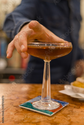 Elegant and sophisticated cocktail served on a professional bar counter. The image features a beautifully garnished drink in a stylish glass, set against a background of blurred liquor bottles
