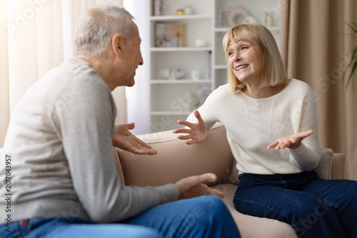 Tableau sur toile Mature couple sitting on a sofa at home, both gesturing with open hands and talk
