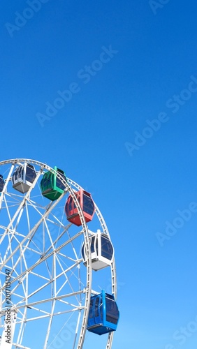 Ferris wheel cabins against blue sky in city amusement park, vertical backdrop with copy space. Children's entertainment, family weekend. Fair or market on sunny day. Symbol of Royal Easter Show