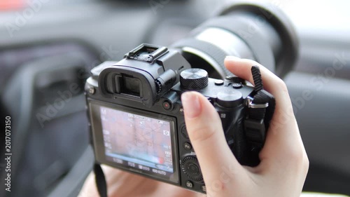 Hand holds camera inside car. View shows rear screen and lens. Focus shifts slightly across frames. Car interior blurred in background. Neutral lighting on equipment. No animals or plants visible