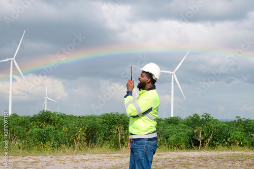 Technician communicating via a walkie talkie, overseeing wind turbines and a rainbow. A symbol of sustainable energy