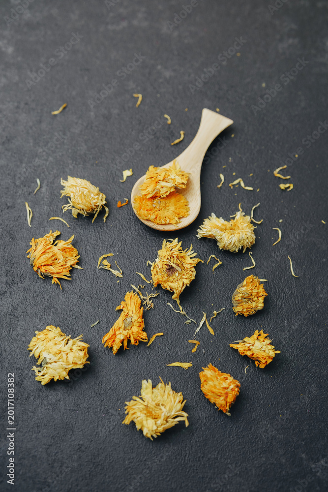 Fototapeta premium Dried chrysanthemums scattered on dark textured surface with wooden spoon