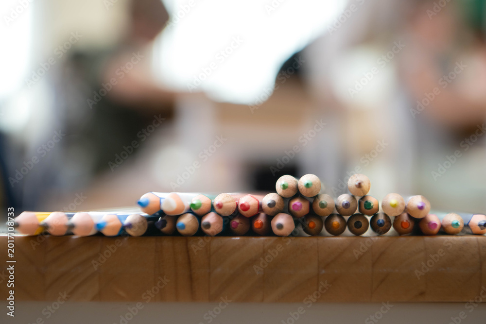 Obraz premium Colored pencils arranged on a wooden table with soft blurred classroom background