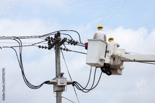Electric utility workers repair and install high voltage power lines from a bucket truck, highlighting electrical maintenance, infrastructure service, safety procedures, and skilled labor.