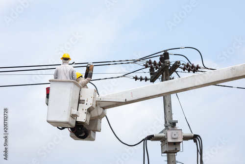 Electric utility workers repair and install high voltage power lines from a bucket truck, highlighting electrical maintenance, infrastructure service, safety procedures, and skilled labor.