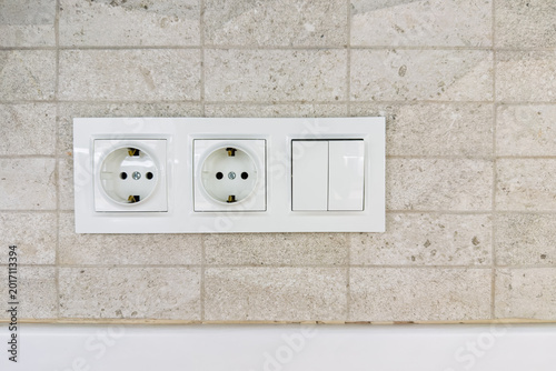 Foto White power outlets and light switches on a textured tiled wall