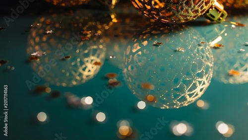 Golden christmas baubles reflecting on a dark teal surface with scattered confetti stars
