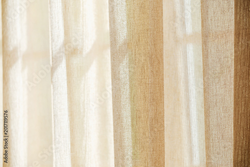 Fotografi Light filtering through textured fabric window drapes creating soft shadows and a warm ambient glow