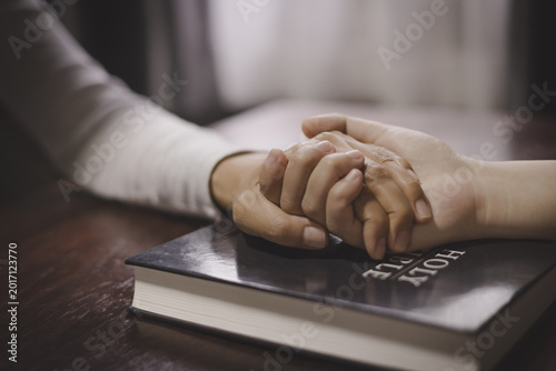 Slika na platnu Christian group of people holding hands praying worships together to believe and Bible on wooden table for devotional for prayer meeting
