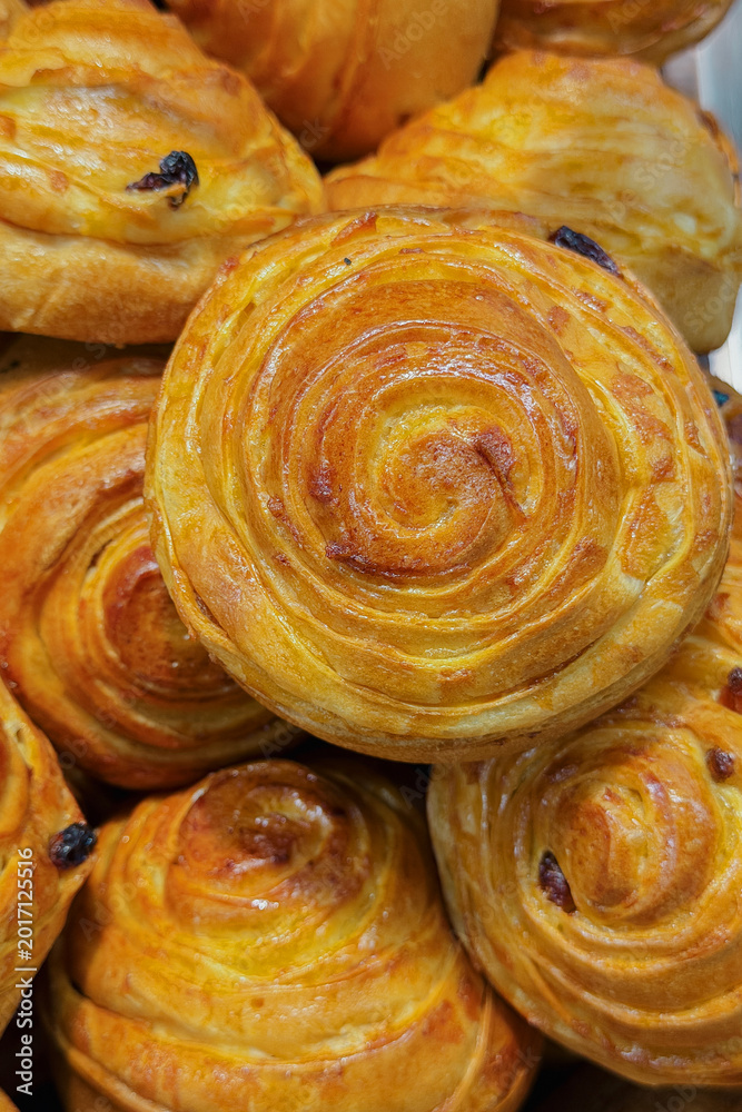Fototapeta premium Close up of delicious golden brown glazed spiral sweet rolls with baked raisins arranged for display