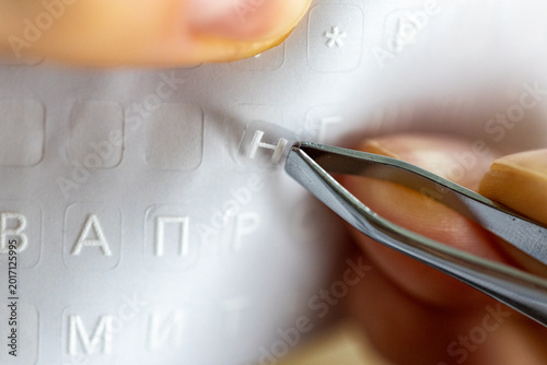 Hands taking and applying letter stickers with tweezers on English keyboard, Cyrillic alphabet characters for multilingual typing