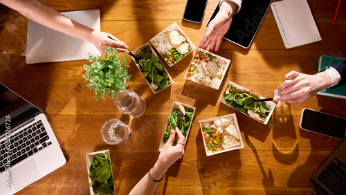 Obraz na plátně Top view of healthy office lunches with coworkers eating at wooden table