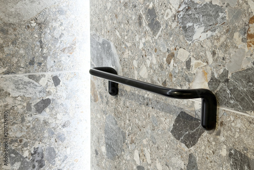 Black metal grab bar mounted on patterned stone wall