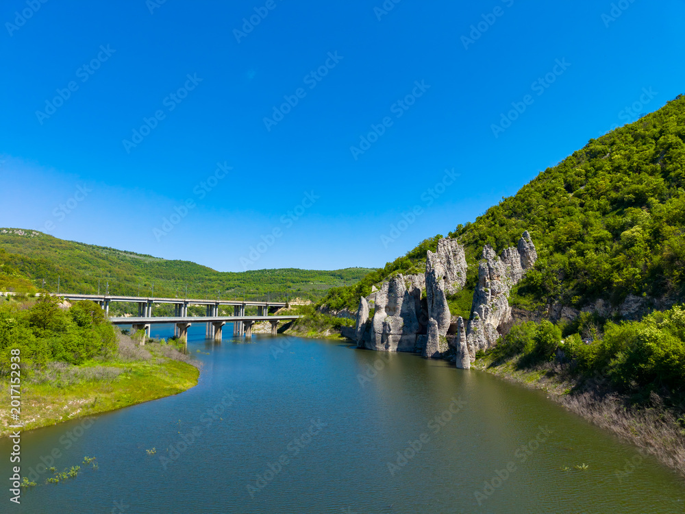 Obraz premium Landscape features a river, rocks, and a bridge in a green valley on a bright day in a rural area