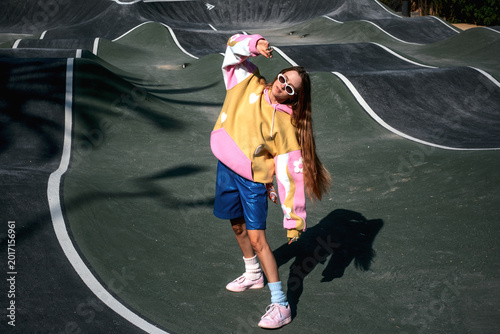 Quadro su tela Young woman posing in colorful hoodie and sunglasses at urban pump track, expres