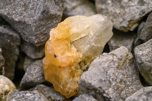 Vászonkép Close-up of a rough, translucent yellow crystal nestled among grey stones