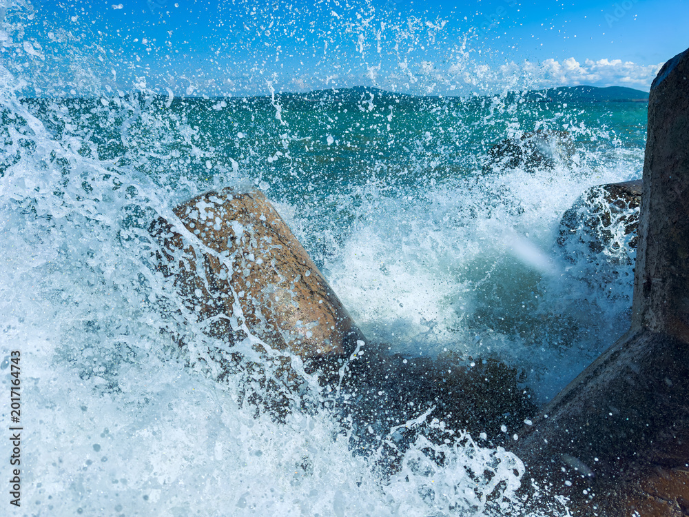 Fototapeta premium Waves crash against rocks by the sea under a clear blue sky in a coastal area in daytime