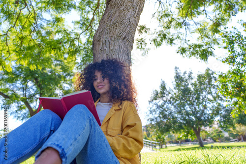 Obraz na płótnie Young woman enjoying nature, reading book, sitting under tree in park, finding i