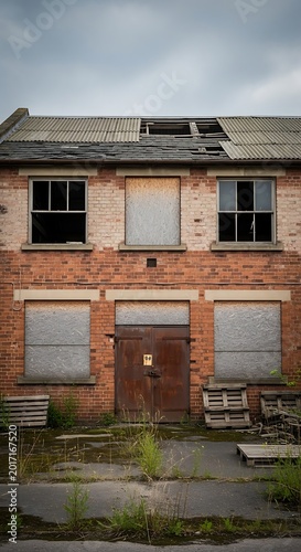 Abandoned Brick Building Standing with Boarded Windows and Damaged Roof in Overgrown Urban Lot