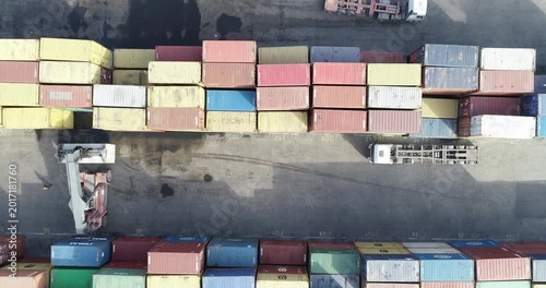 Aerial view of a container port terminal. Colorful cargo containers stacked in rows with a reach stacker and a truck, illustrating the concept of global trade, logistics, and supply chain.