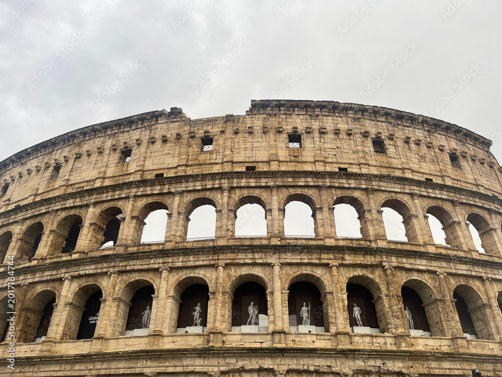 Fototapeta premium Iconic Roman Colosseum Exterior Under Dramatic Cloudy Sky in Rome Italy