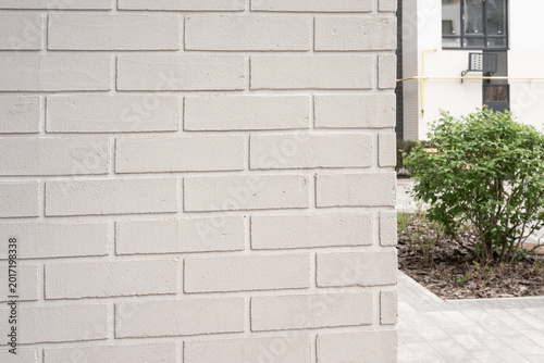 Light grey painted brick wall texture creating a modern architectural facade with building and plant background