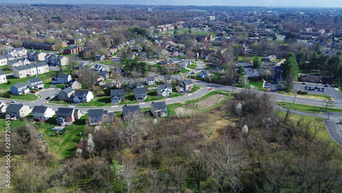 Roaddivided residential zone west of Paper Mill Rd near White Clay Creek transitions toward mixed suburban corridors. Dark roofs, solar panels, open grassland, soft spring tones, Newark, DE