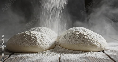 Flour being poured over freshly kneaded dough on a wooden surface in a dimly lit kitchen
