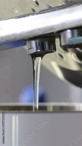Clear water pouring from chrome spout into electric kettle, kitchen appliance close up. Vertical